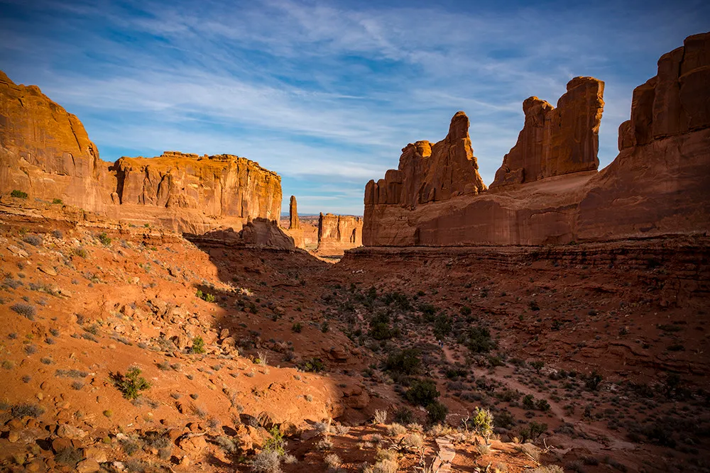 A wide desert canyon flanked by tall red sandstone fins and walls under a clear blue sky