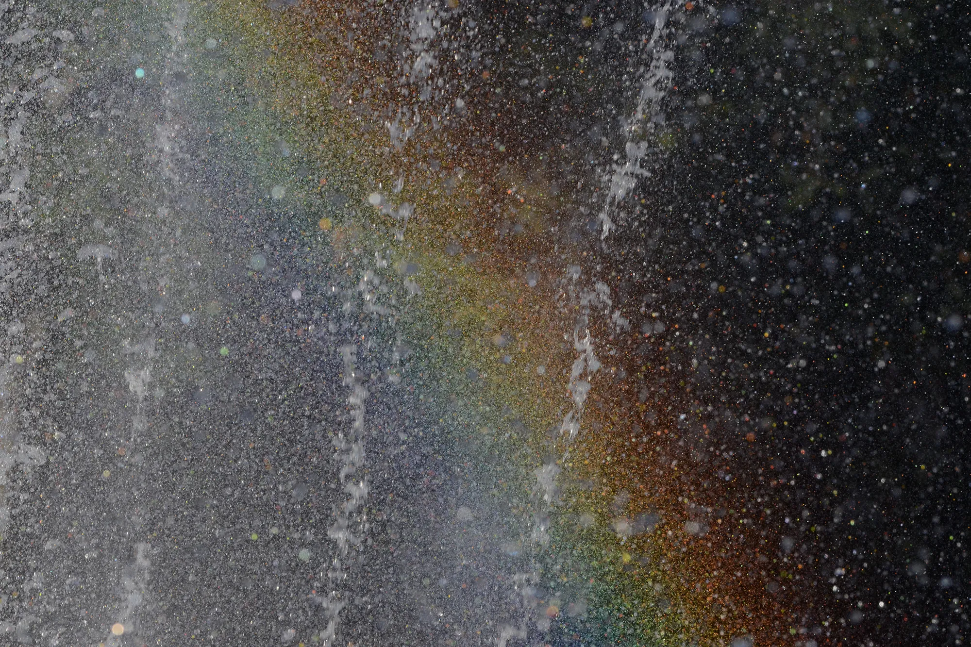 Fine droplets of falling water catching sunlight and splitting it into a soft band of rainbow color